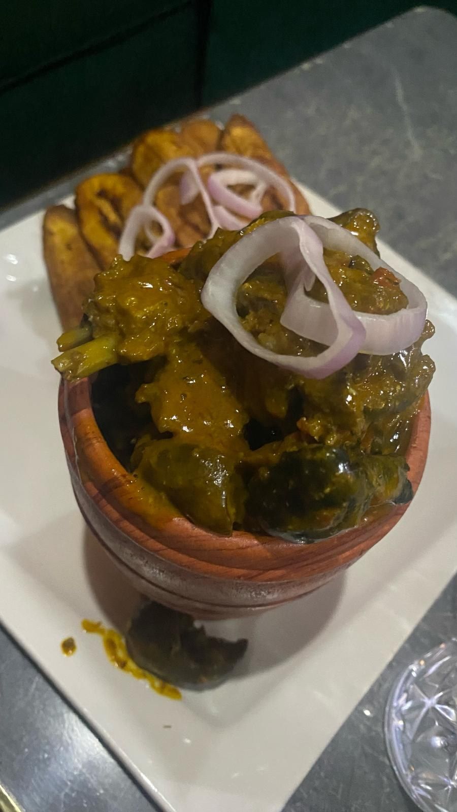 Soup served in a clay pot with onion rings and fried plantain