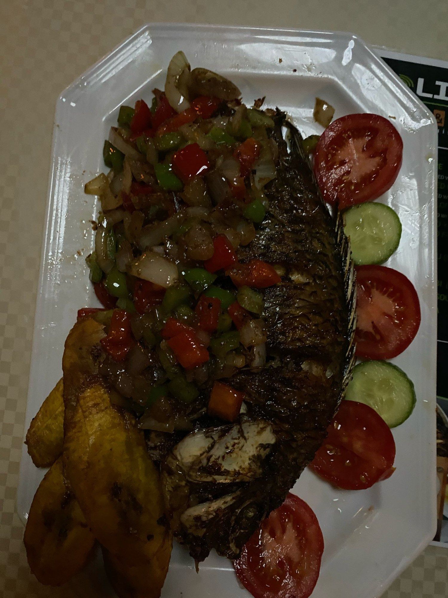 Whole grilled fish topped with diced peppers and onions, with plantain and tomato