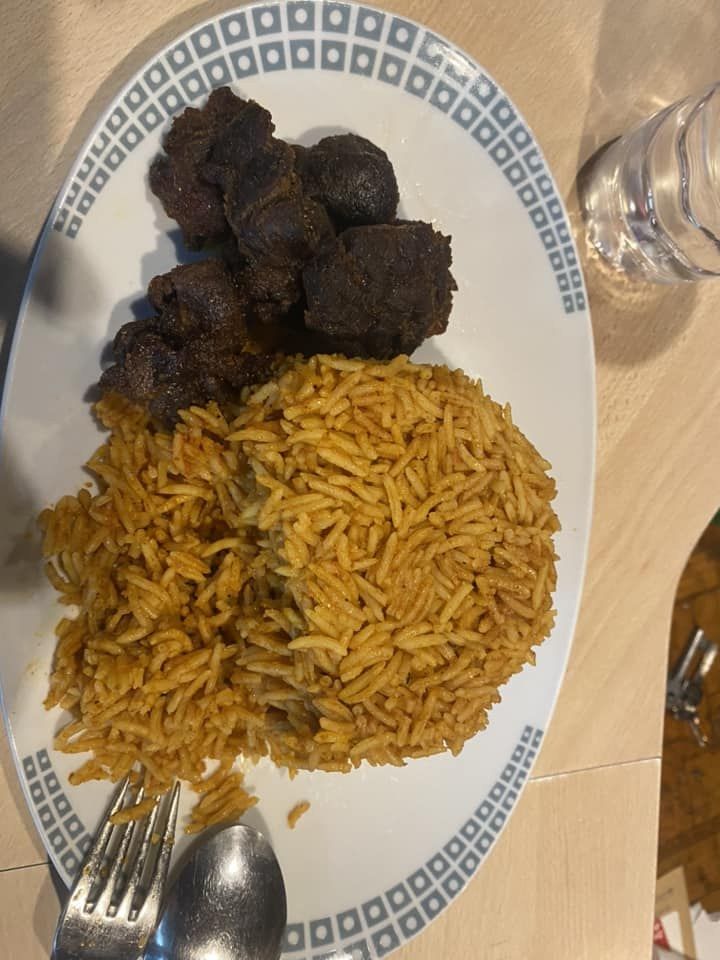 Jollof rice with pieces of fried meat on a white plate
