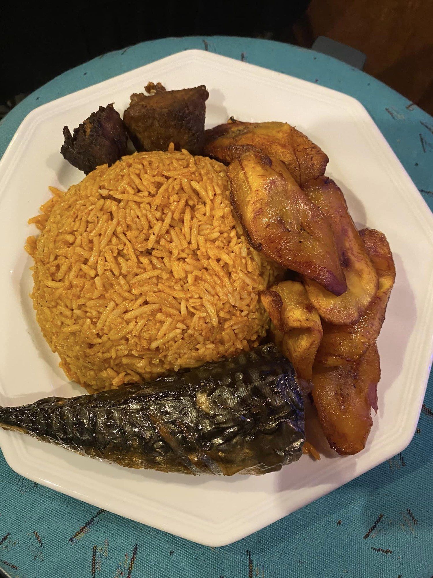 Jollof rice with fried plantain and fish on an octagonal plate